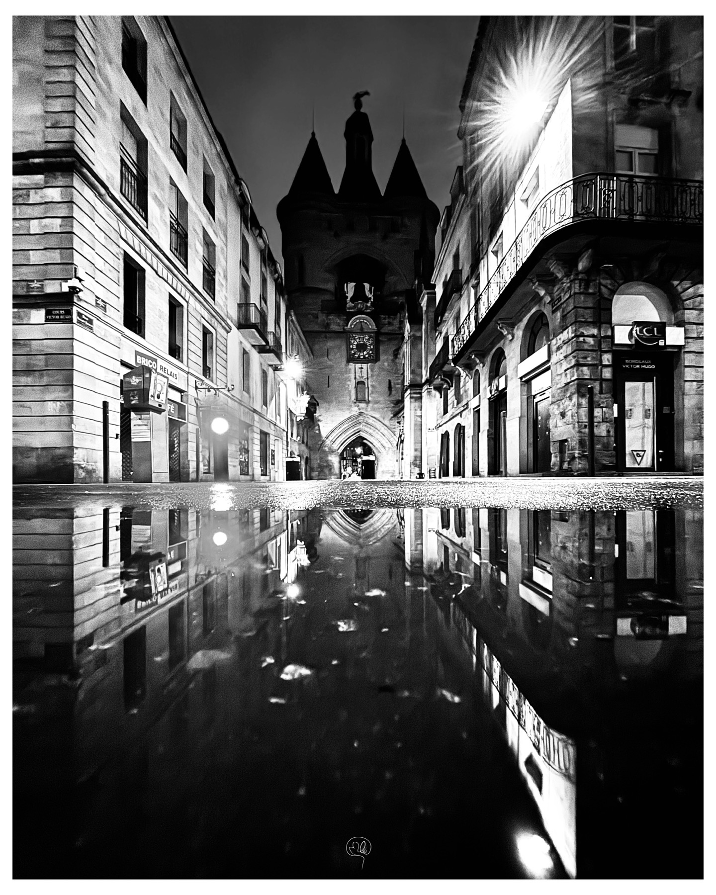 A Bordeaux street, medieval gate and façades reflected in a puddle