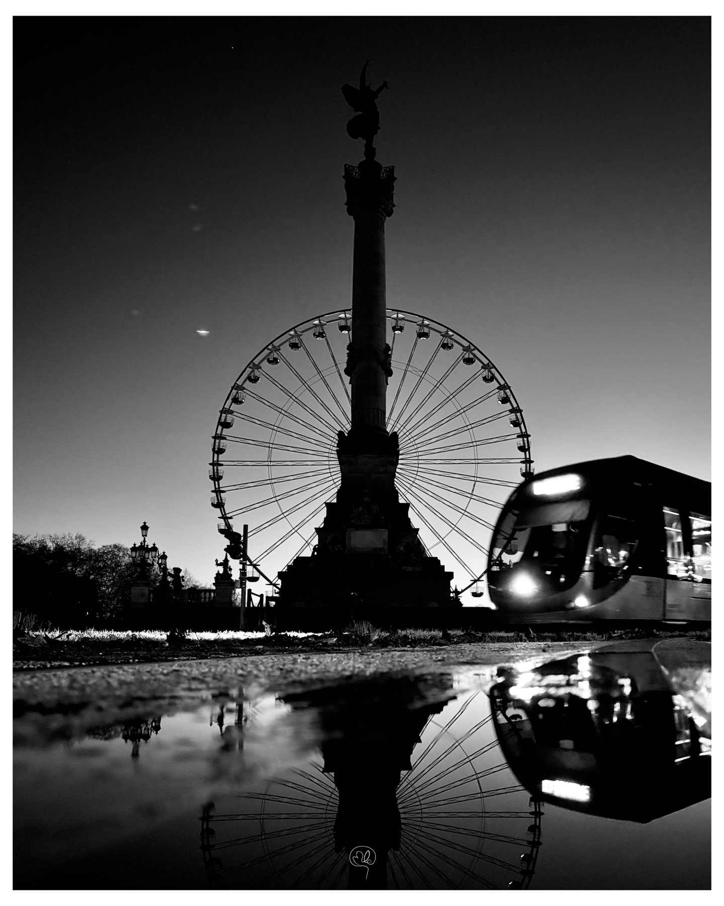 Grande roue, colonne et tramway se reflétant dans une flaque nocturne